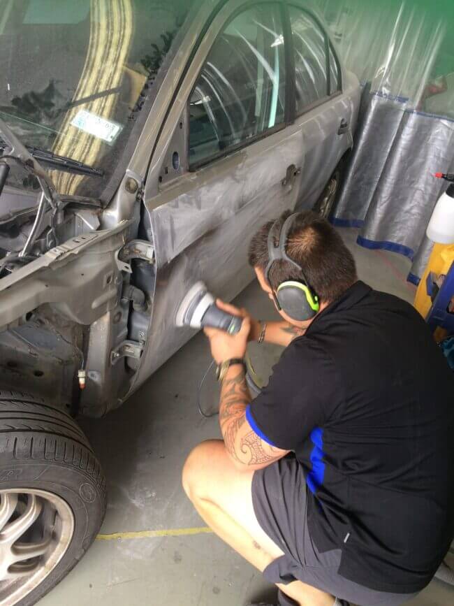 Panel beater sanding a vehicle panel